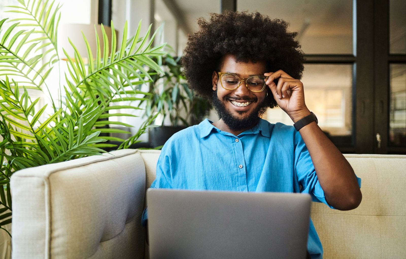 Young man smiling at his laptop on the couch at home