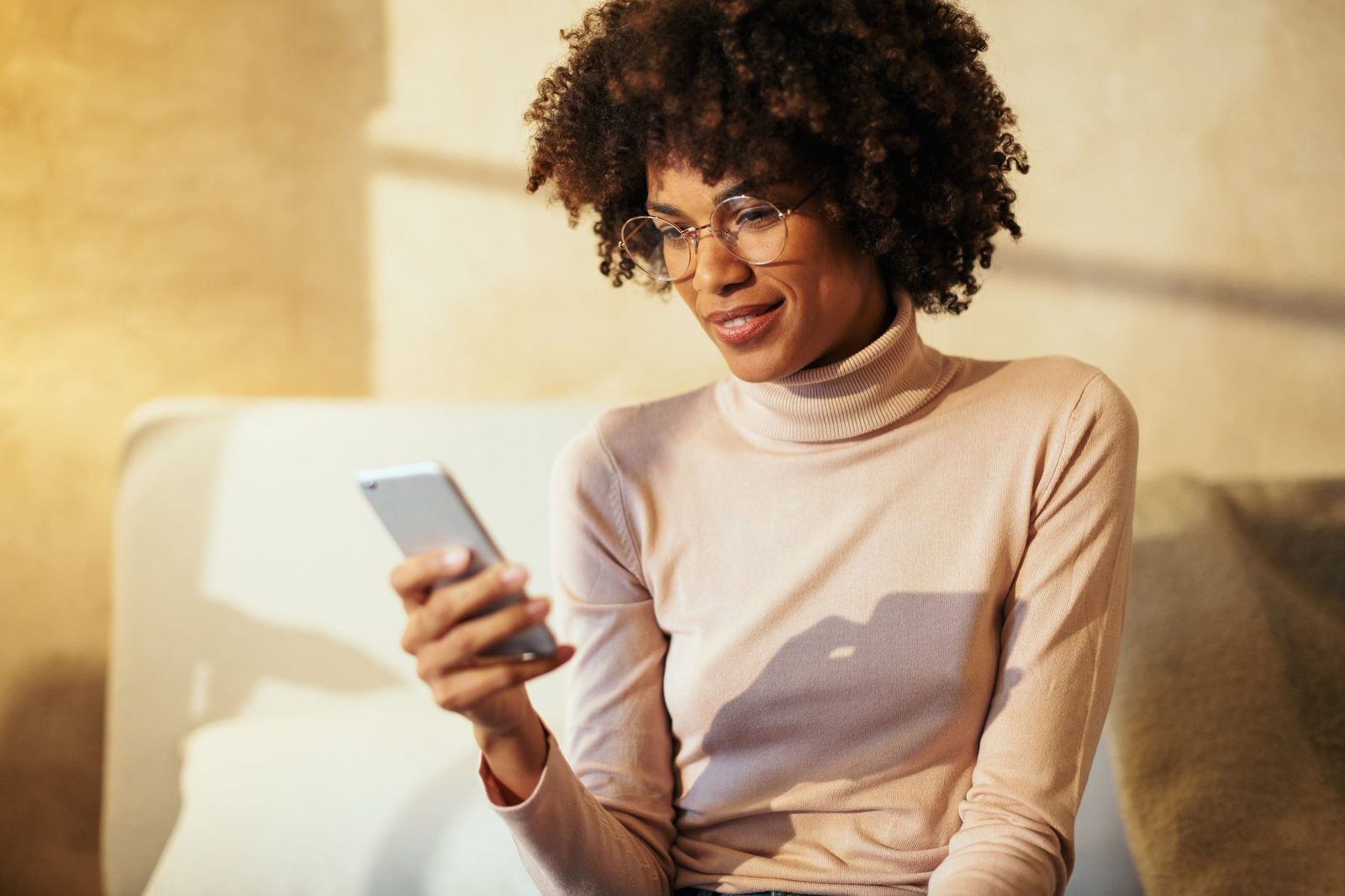 Woman smiling at her phone at home in warm afternoon light